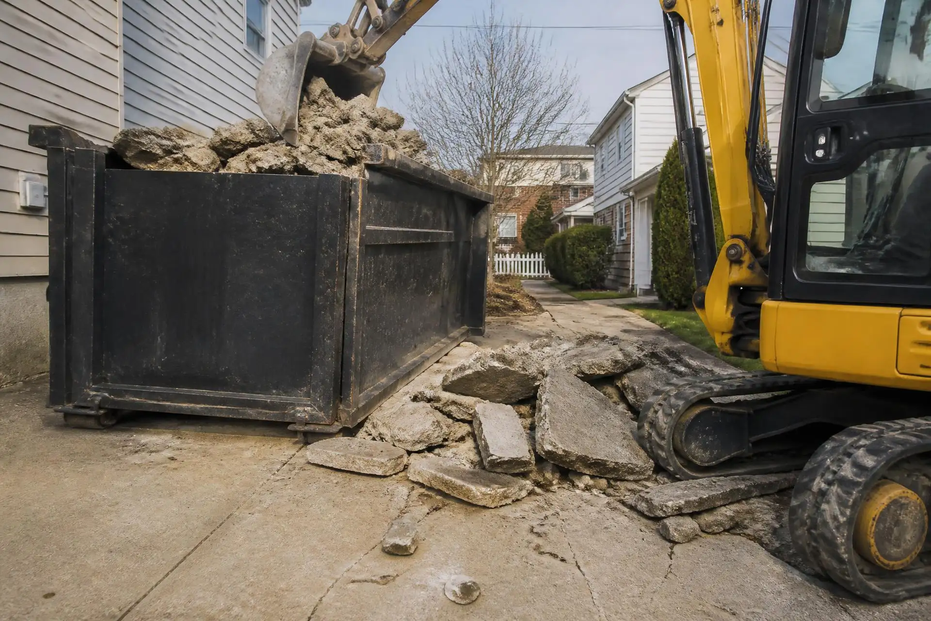 Mini excavator loading broken concrete driveway slabs into a heavy-duty container